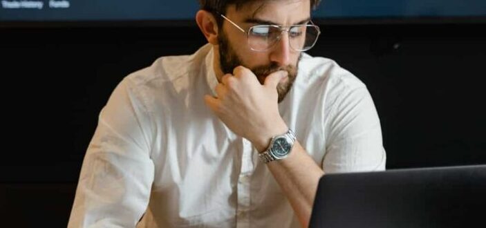 person in glasses pensively looking at laptop